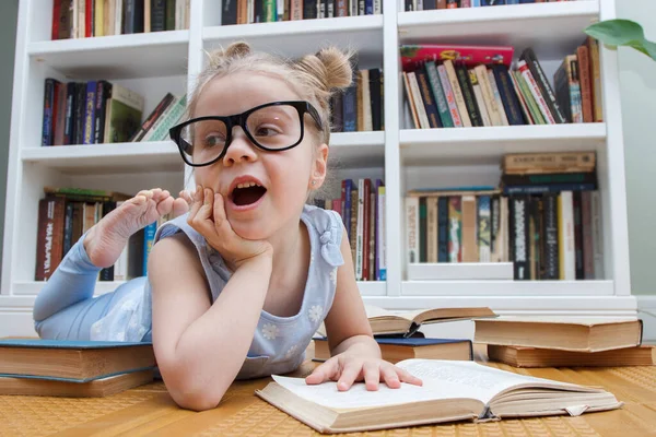 戴眼镜的可爱小女孩坐在书架上的前面 图书馆的教育概念 — 图库照片