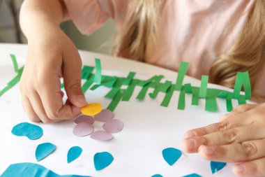 Sevimli çocuk renkli kâğıt ve yapıştırıcılı bir cihaz yapıyor. Hobi ve eğitim kavramı