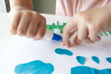 Sevimli çocuk renkli kâğıt ve yapıştırıcılı bir cihaz yapıyor. Hobi ve eğitim kavramı