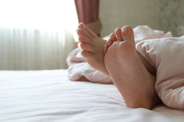 Feet under a light blanket on the bed. Concept of sleeping or waking in the morning