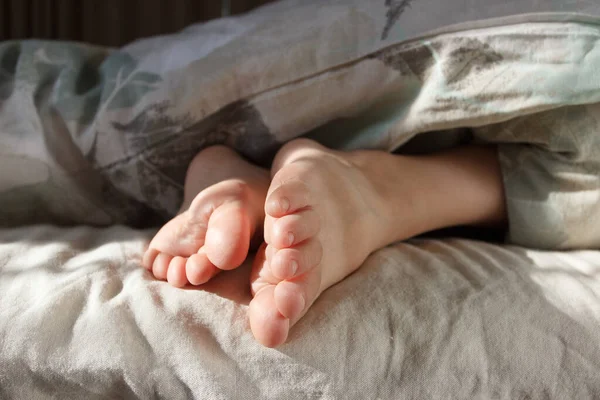 Feet under a light blanket on the bed. Concept of healthy life