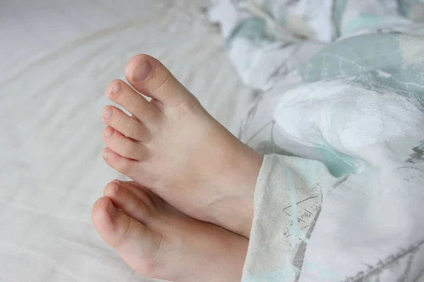 Feet under a light blanket on the bed. Concept of health and life style