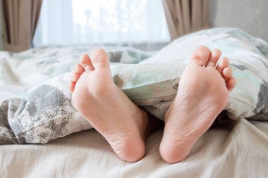 Ayaklar hafif bir battaniyenin altında, yumuşak bir odak arka planı var. Sağlık kavramı