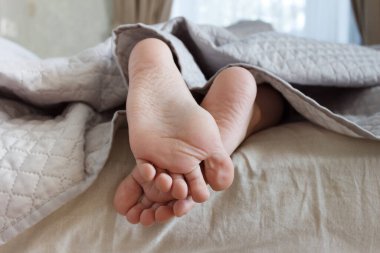 Ayaklar hafif bir battaniyenin altında, yumuşak bir odak arka planı var. Sağlık kavramı