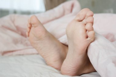 Ayaklar hafif bir battaniyenin altında, yumuşak bir odak arka planı var. Sağlık kavramı