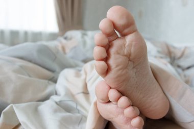 Ayaklar hafif bir battaniyenin altında, yumuşak bir odak arka planı var. Sağlık kavramı
