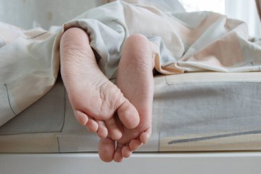 Ayaklar hafif bir battaniyenin altında, yumuşak bir odak arka planı var. Sağlık kavramı