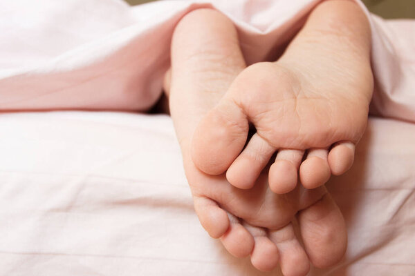 Feet under a light blanket on the bed, soft focus background. Concept of health