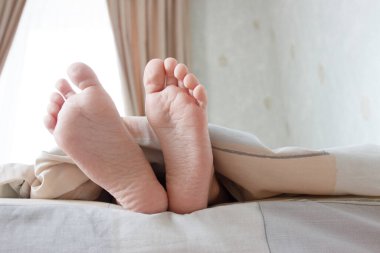 Ayaklar hafif bir battaniyenin altında, yumuşak bir odak arka planı var. Sağlık kavramı