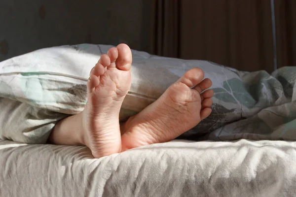 Feet under a light blanket on the bed. Concept of healthy life