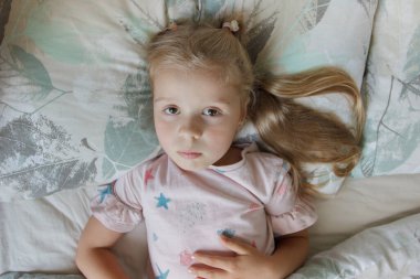 Yatakta yatan küçük tatlı kız. Sabah uyanma kavramı, yumuşak odak arkaplanı