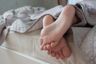 Feet under a light blanket on the bed, soft focus background. Concept of healthy life clipart