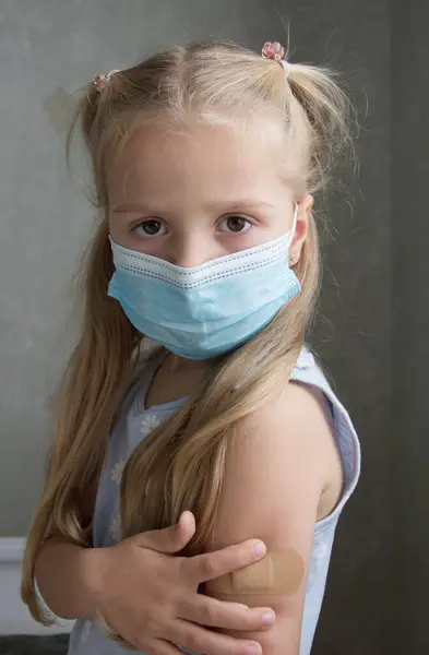 マスクの中の小さな女の子は 皮膚にプラスターが付いている腕を保持します ワクチン接種と予防接種の概念 — ストック写真