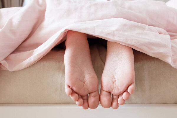 Feet under a light blanket on the bed, soft focus background. Concept of healthy life
