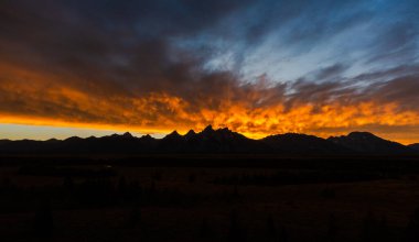 Gün ışığı soluyor, engin bir dağ manzarası üzerine çarpıcı günbatımı renkleri bırakıyor, dramatik gökyüzü, gölge ve doku doğanın huzur dolu, manzaralı güzelliğini vurguluyor.