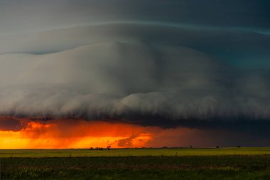 Kaygı verici karanlık şiddetli fırtına, gölgeler, doku ve karamsar atmosferle dolu dramatik bir gökyüzü yaratarak, rengarenk bir gün batımı altında hızla yaklaşır. Güzellik, tehlike ve destansı hava sahnesi harmanlanır.