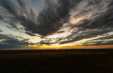 Gün batımının renkleri, sakin tarım arazileri üzerine gökyüzündeki huzurlu bulutları dolduruyor. Yumuşak dokusu, nazik hareketi ve doğanın dingin güzelliği ile kasvetli bir atmosfer yaratıyor.