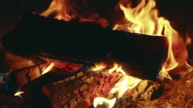 Açık havada yanan odun ateşinde dans eden alevlerin yakın görüntüsü, parlayan közler, yanan odun, yükselen duman ve ışıldayan ısı doğal gece sahnesini aydınlatıyor.