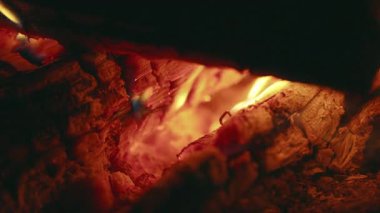 Açık havada yanan odunların detaylı görüntüleri. Parlayan közler, yükselen duman ve titreyen alevler huzurlu gece havasında sıcaklık ve ışık yaratıyor.