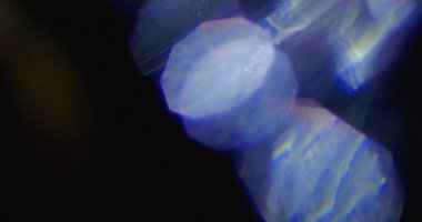 Prizmatik yansımalı bulanık mavi kristal şekiller ve koyu arkaplanda yanardöner parıltılar. Bokeh etkisi mevcut.