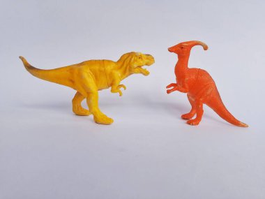 İki dinozor figürü, bir Tyrannosaurus Rex ve bir Parasaurolophus, beyaz arka planda karşı karşıya..