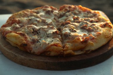 Lezzetli et severler pizzasını ahşap tabakta kapayın. Gün batımında plajda pizza.