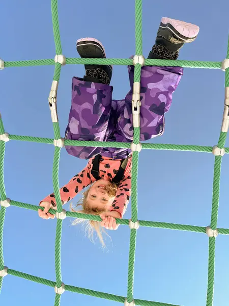 Ilık bir kış gününde, parlak mavi, güneşli bir arka plandan korkmadan bir halat yapısına tırmanan kız.