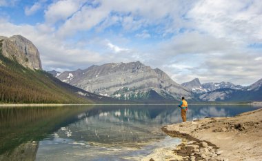 Kananaskis, Alberta, Kanada - 09 / 10 / 2024: Dağlar, deniz mavisi göller ve yemyeşil ağaçlarla çevrili bir göl gibi sakin bir camda balık tutan bir adam