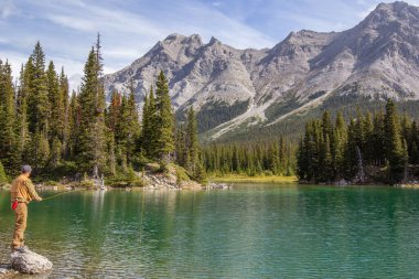Kananaskis, Alberta, Kanada - 09 / 10 / 2024: Sıcak güneşli bir günde, arka planda daima yeşil ağaçlar ve dağlar olan açık deniz sularında uçan bir adam