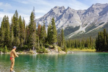Kananaskis, Alberta, Kanada - 09 / 10 / 2024: Sıcak güneşli bir günde, arka planda daima yeşil ağaçlar ve dağlar olan açık deniz sularında uçan bir adam