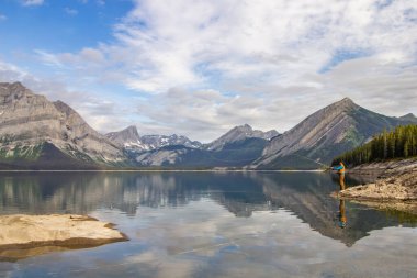Kananaskis, Alberta, Kanada - 09 / 10 / 2024: Dağlar, deniz mavisi göller ve yemyeşil ağaçlarla çevrili bir göl gibi sakin bir camda balık tutan bir adam