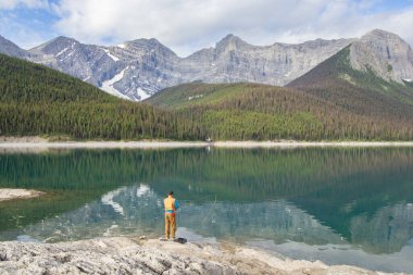 Kananaskis, Alberta, Kanada - 09 / 10 / 2024: Dağlar, deniz mavisi göller ve yemyeşil ağaçlarla çevrili bir göl gibi sakin bir camda balık tutan bir adam