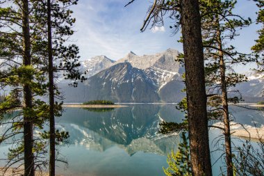 Arka planda kar kaplı kayalık dağcıların manzarası. Güneşli bir günde, deniz mavisi bir gölün ortasında küçük bir ada.