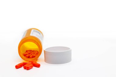 Generic red pills laying in front of pill bottle on white background with lid and free space clipart