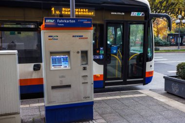 Wiesbaden, Hessen Almanya-10-08-2023: Ön planda bir bilet makinesiyle otobüs durağına gelen elektrik otobüsü.