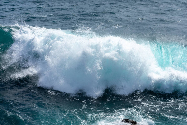 Idyllic scene of clear blue sea crashing against volcanic black rocks along the cliffs of Terceira Island, Azores.