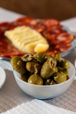 Bir tabak canlı yeşil zeytin geleneksel Alentejo peyniri ve pişirilmiş sosis zeminine karşı hazırlanır. Sahne, Portekiz mutfağının özünü samimi bir restoranda yakalıyor..