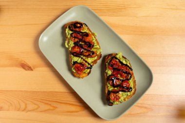 Restoran masasında üzerinde canlı guacamole ve vişneli domatesler bulunan bir tabak bruschetta. Altın tost ekmeği taze yeşil guacamole ve kırmızı domateslerle çok güzel tezat oluşturuyor..