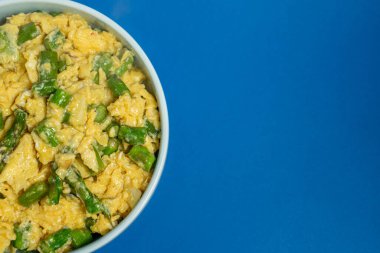 Canlı yeşil kuşkonmazla karıştırılmış çırpılmış yumurta içeren geleneksel bir Alentejo yemeği. Yumurtaların altın renkleri, koyu mavi arka planla çok güzel tezat oluşturuyor..