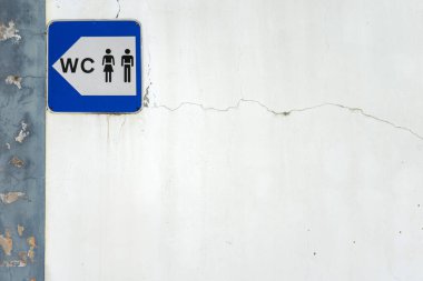 Bir şehirdeki umumi tuvaletlerin yerini gösteren basit bir mavi beyaz tabela. Bir erkek ve dişi ikonu gibi klasik bir sembolle açık ve kalın harfler gösteriyor..