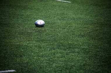Yeşil çayırda rugby topu, harekete hazır. Dinamik kompozisyon oyunun özünü yakalar.
