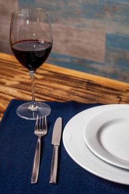 Çatal ve bıçak mavi bir tabağın yanında, bir bardak kırmızı şarapla, bir restoran masasında..