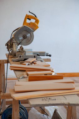 Bir masa testeresi, ahşap döşeme tahtaları kesim için yerleştirilmiş. Sahne döşeme kurulumunun hazırlık aşamasını yakalıyor, araçlar ve malzemeler vurgulanıyor.