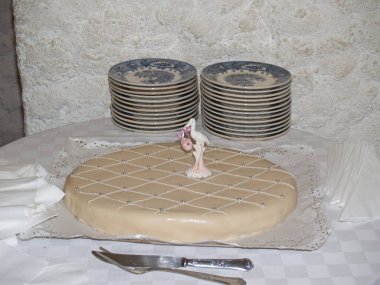 A christening cake on a restaurant table, featuring a figurine of a stork holding a pink bundle with a baby inside, symbolizing the baptism of a baby girl. clipart