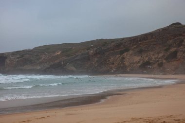 Monte Clrigo beach in Aljezur, Portugal, on a foggy morning. Seagulls take flight from the sandy shore, creating a serene and mystical coastal scene. clipart