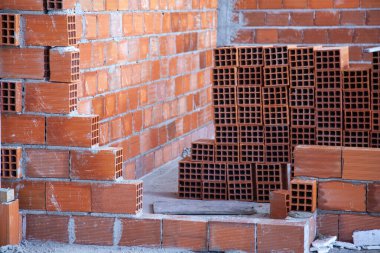 Yeni inşa edilmiş tuğla duvar sağlam duruyor. Arka planda kullanılmamış tuğlalar var. Gelecekteki inşaata hazır.. 