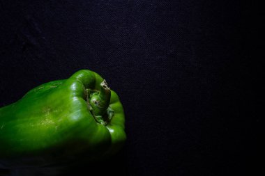 Canlı yeşil bir dolma biber, siyah bir zemin üzerinde izole edilmiş, taze, parlak derisini ve taze dokusunu sergiliyor. Mutfak, tarım veya sağlık temalı projeler için mükemmel.