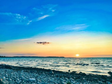 Alacakaranlık sonrası alacakaranlık büyüleyici bir atmosfer yaratıyor. Güneş ışığı suyun sıvı yüzeyinden yansıyor. Mavi gökyüzü ve kabarık bulutlarla birleşiyor.