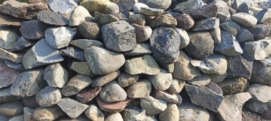 Nehrin kıyısında düzgünce dizilmiş orta büyüklükteki taşlar koleksiyonu.