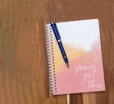 Tahta masadaki mavi kalem ve not defteri motive edici kelimelerle.